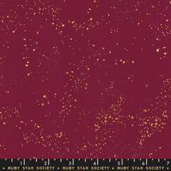 Pattern of multi-colored speckles on a dark red background with ruler